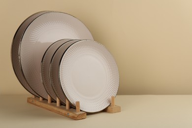 Drying rack with beige ceramic plates on pale yellow table, space for text