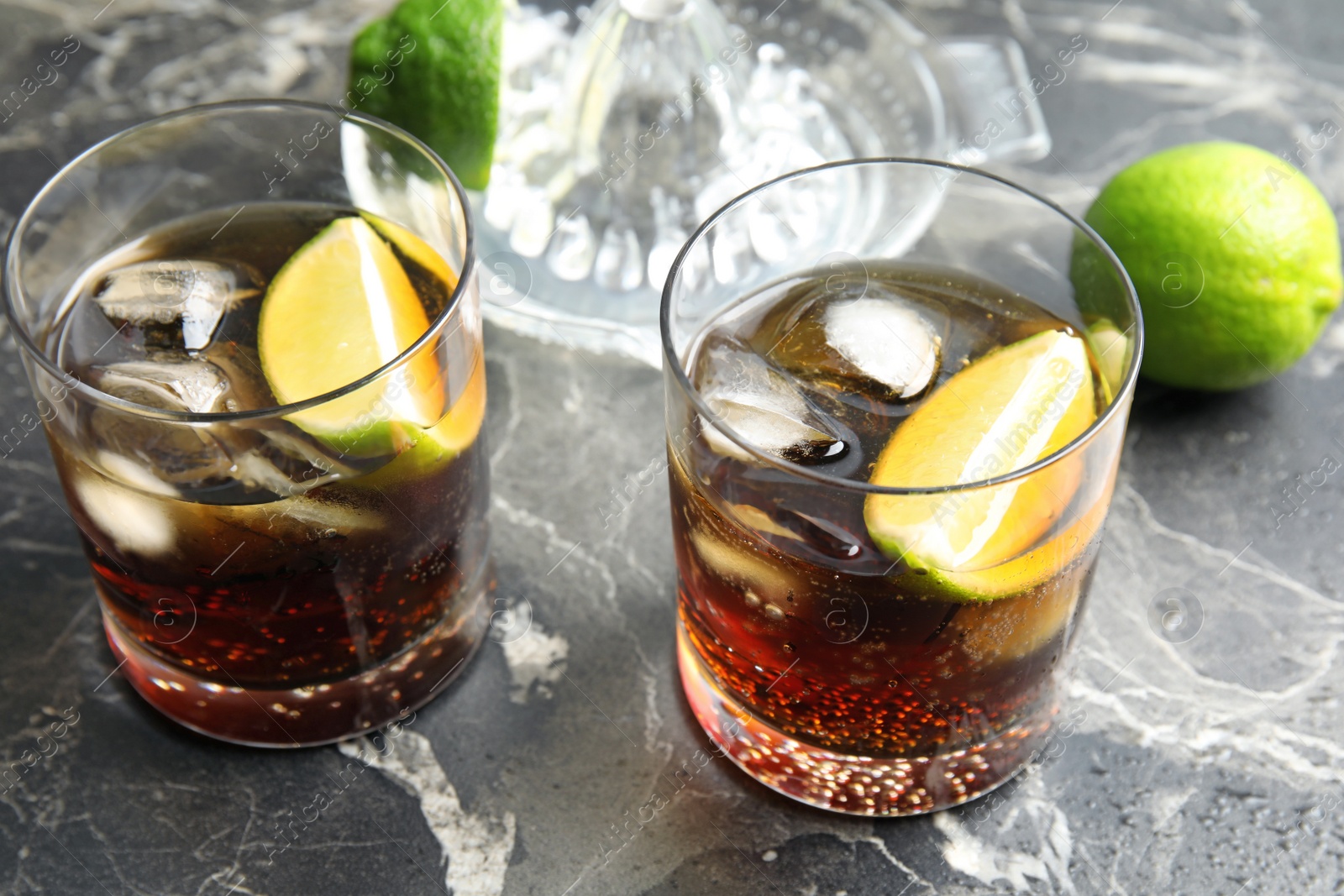 Photo of Glasses of cocktail with cola, ice and cut lime on marble background