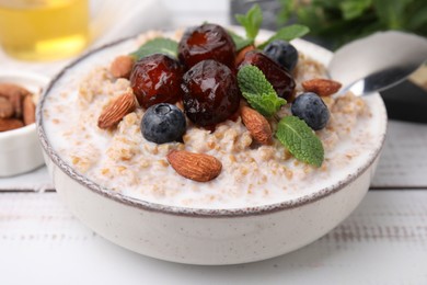 Photo of Tasty wheat porridge with milk, dates, blueberries and almonds in bowl on light wooden table, closeup