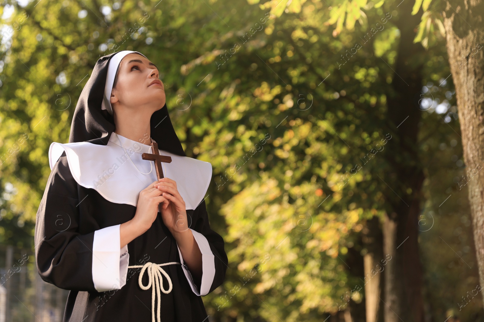 Photo of Young nun with Christian cross in park on sunny day, space for text