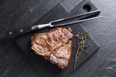 Photo of Delicious fried beef meat, thyme, peppercorns and fork on black table, top view