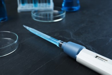 Photo of Laboratory analysis. Micropipette with liquid and petri dishes on black table, closeup