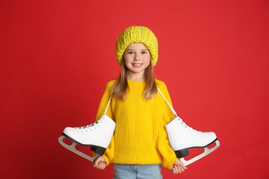 Photo of Cute little girl in yellow knitted sweater with skates on red background