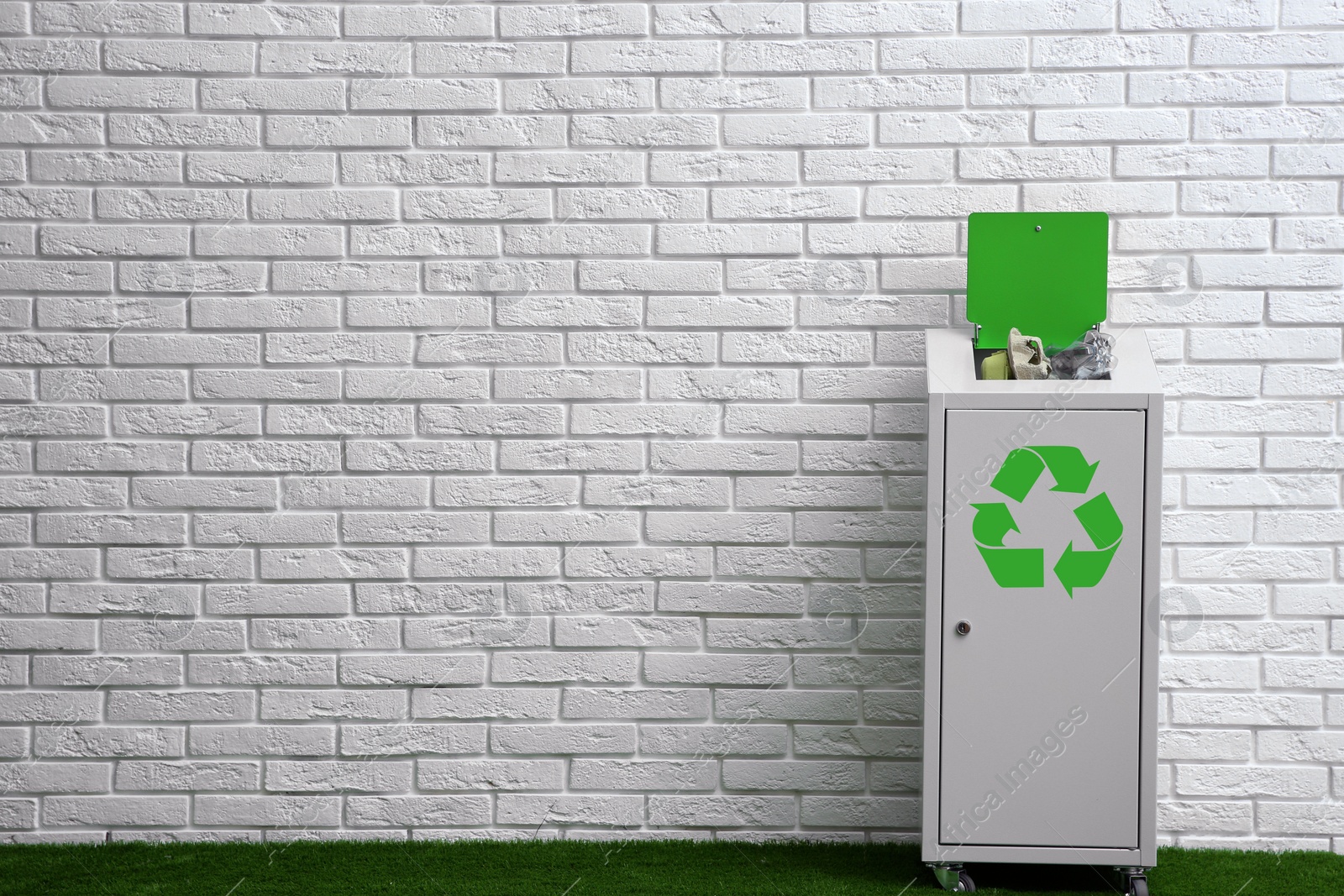 Photo of Overfilled trash bin with recycling symbol near brick wall indoors. Space for text