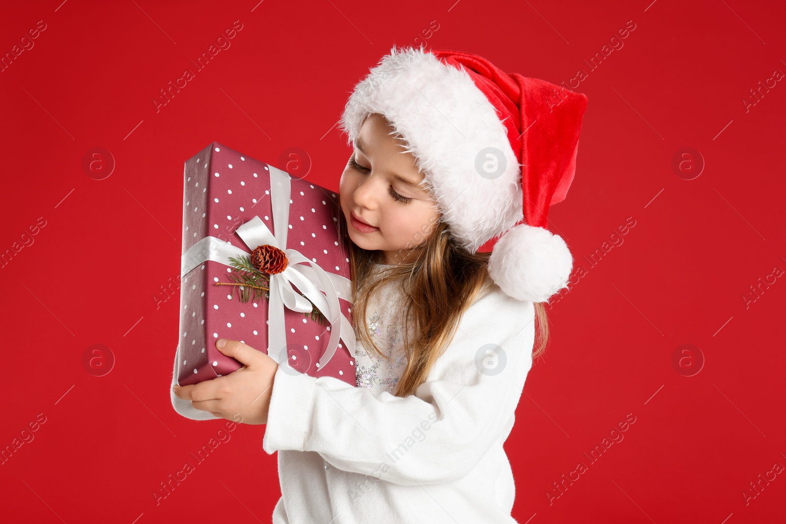 Photo of Cute child in Santa hat with Christmas gift on red background