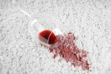 Photo of Overturned glass and spilled exquisite red wine on soft carpet