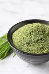 Wheat grass powder in bowl on white table, closeup