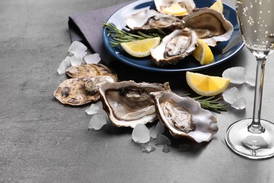 Photo of Fresh oysters with lemon, rosemary and glass of champagne on grey table