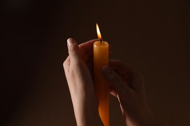 Photo of Woman holding burning church candle on dark background, closeup