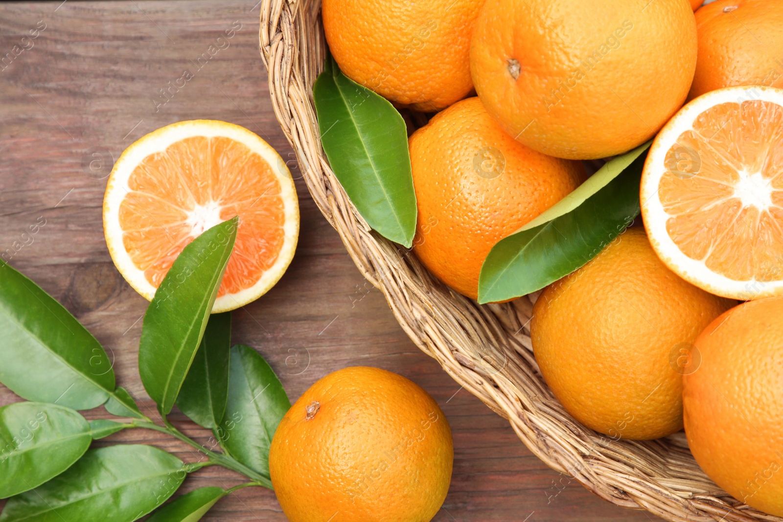 Photo of Wicker basket, ripe juicy oranges and green leaves on wooden table, flat lay