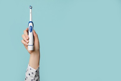 Woman holding electric toothbrush on light blue background, closeup. Space for text