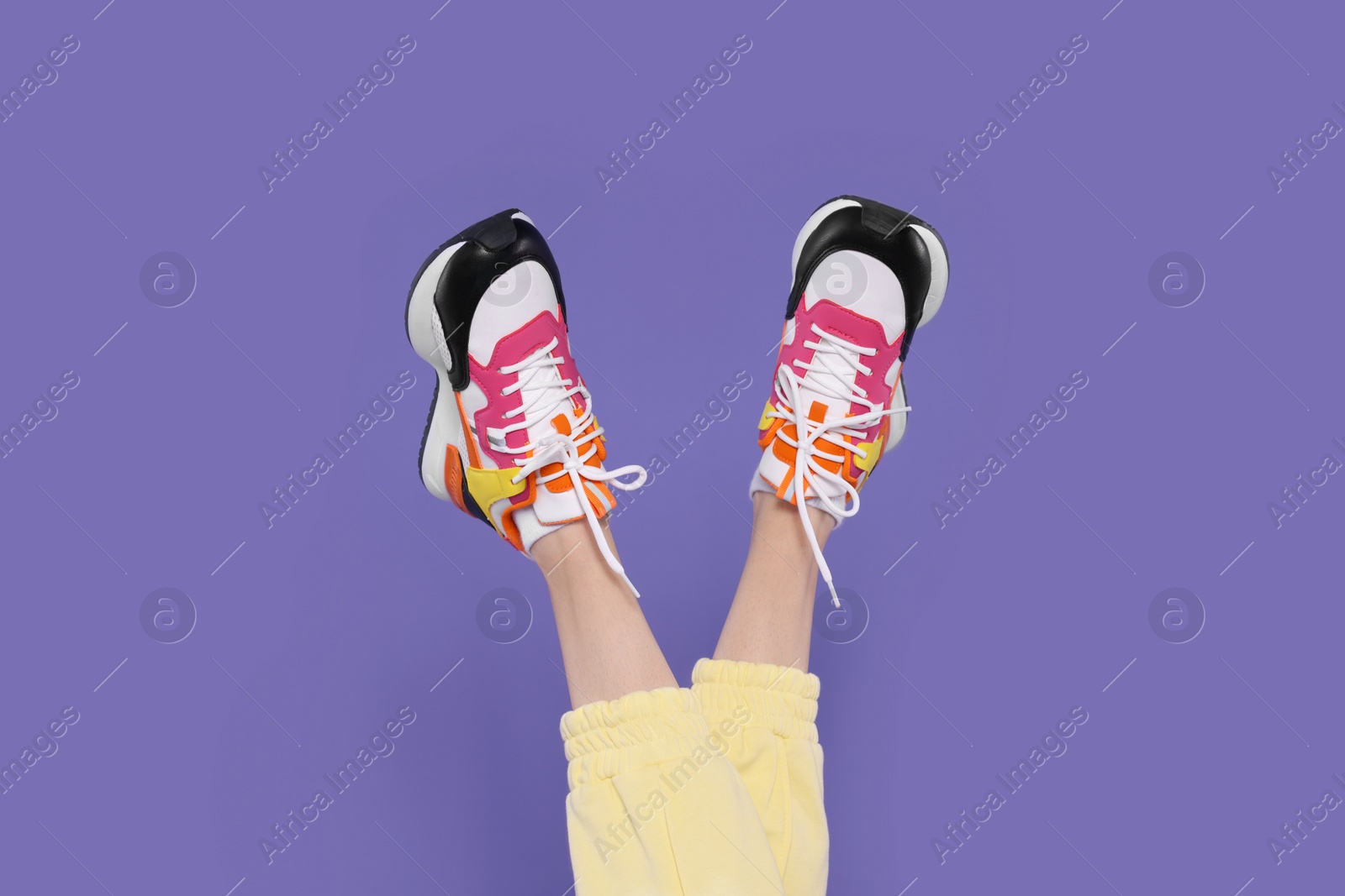 Photo of Woman wearing pair of new stylish sneakers on purple background, closeup
