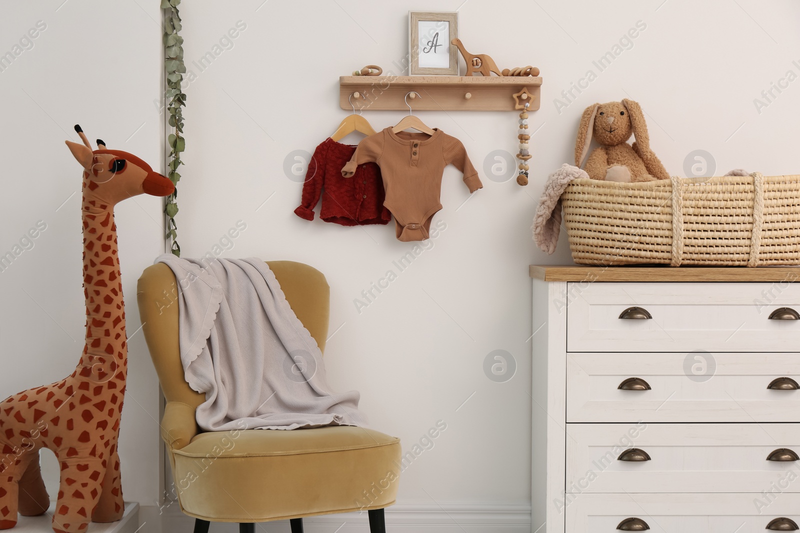 Photo of Wooden shelf with baby clothes, toys and furniture in room. Interior design