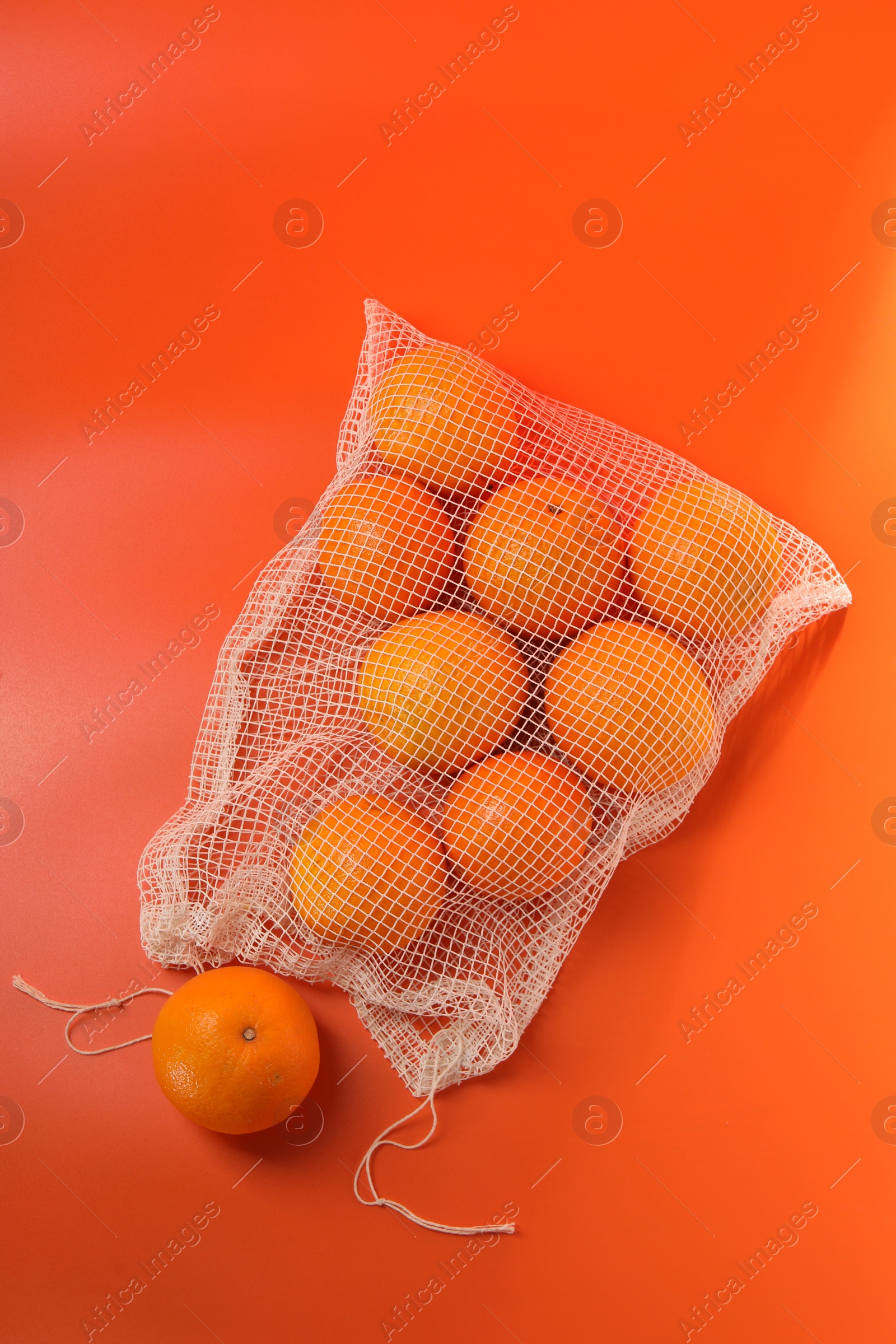 Photo of Net bag with fresh oranges on color background, top view