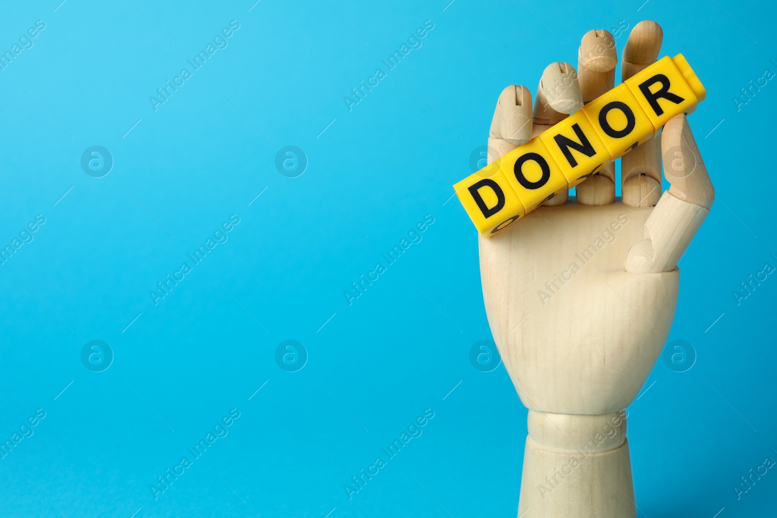 Photo of Mannequin hand holding word Donor made of cubes on light blue background. Space for text