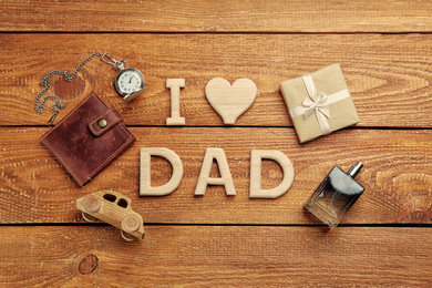 Photo of Phrase I LOVE DAD made of wooden letters and male accessories on wooden table, flat lay. Happy Father's Day