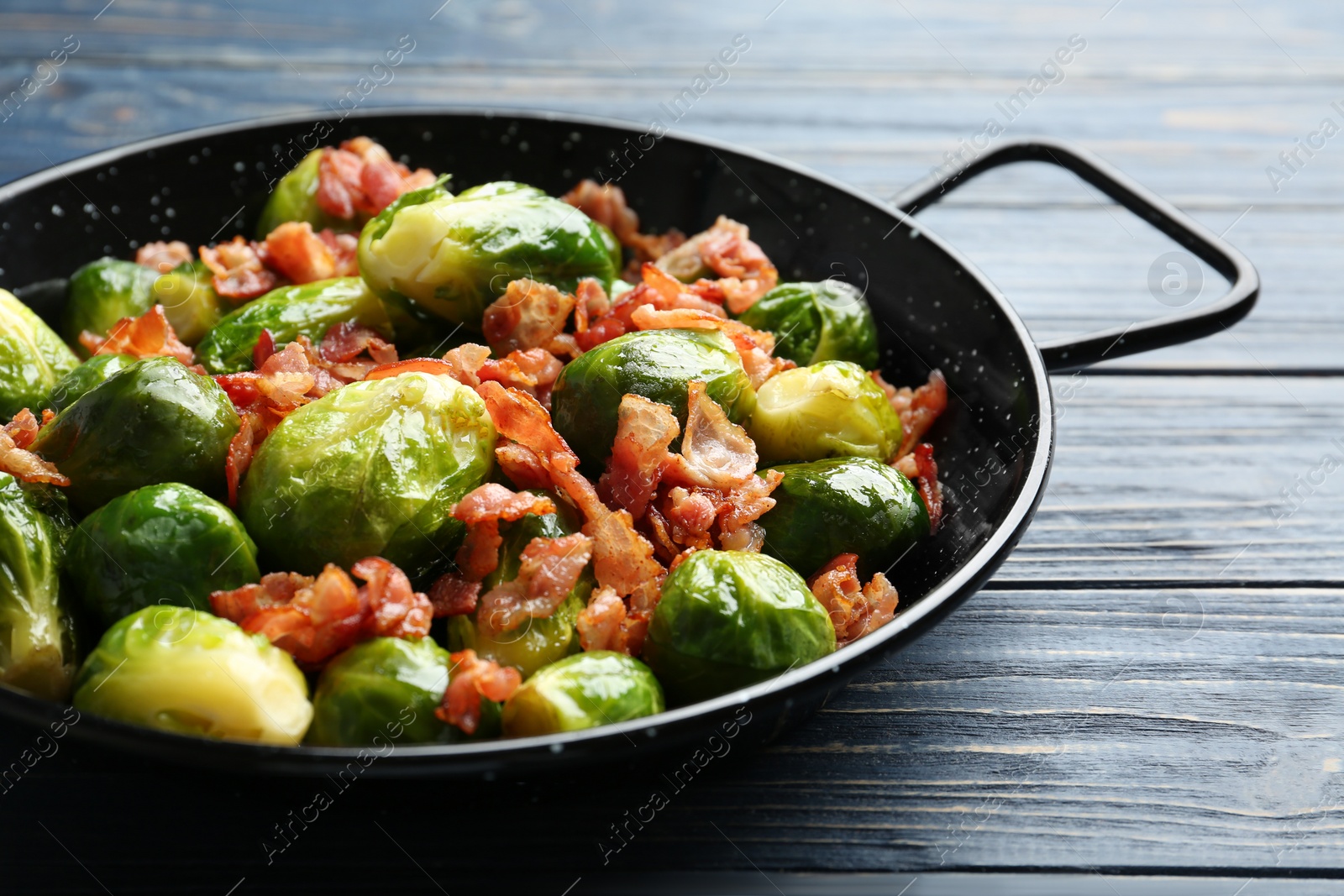 Photo of Tasty roasted Brussels sprouts with bacon on blue wooden table, closeup