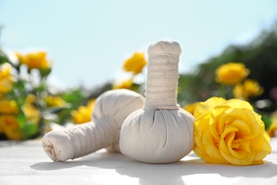 Photo of Spa massage herbal bags with yellow rose on white table in blooming garden. Harmony and zen