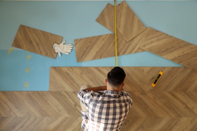 Photo of Professional worker installing new parquet flooring indoors, top view