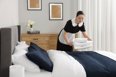 Maid putting stack of towels onto bed in hotel room