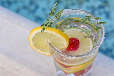 Photo of Delicious refreshing lemonade with raspberries near pool, closeup