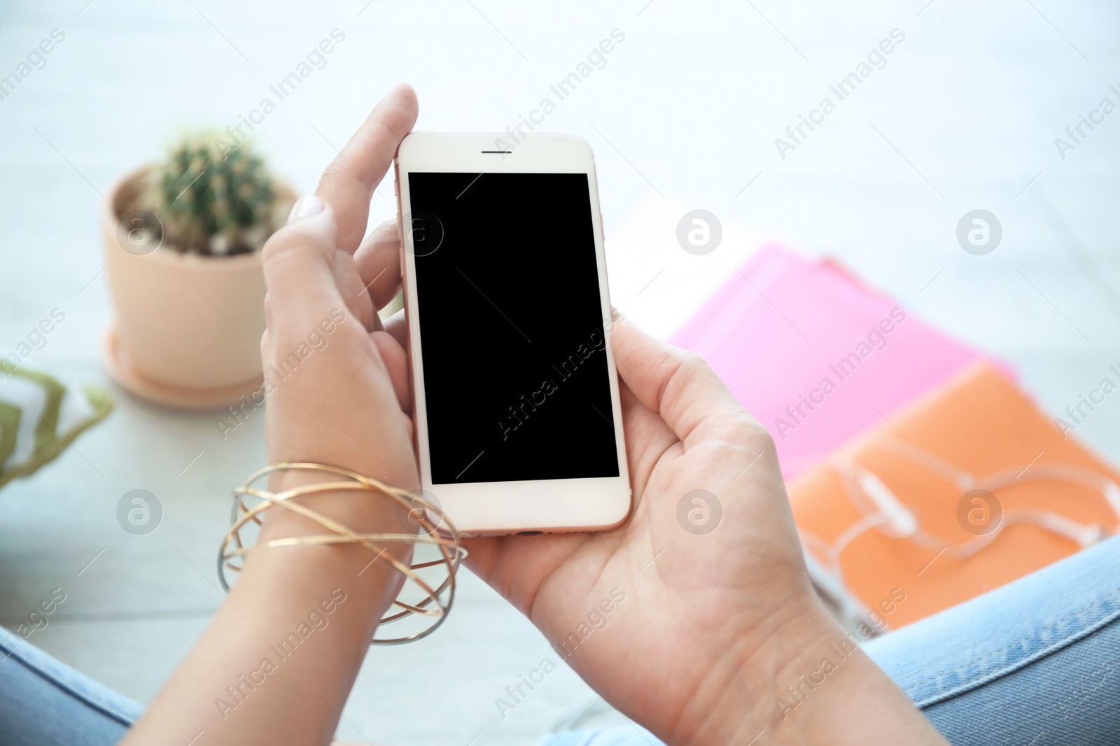 Photo of Young woman holding mobile phone with blank screen in hands, indoors