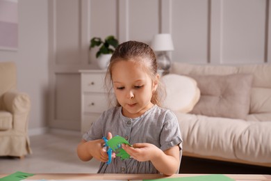 Photo of Little girl cutting color paper with scissors at table indoors