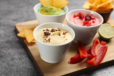 Different kinds of tasty hummus with ingredients on grey table