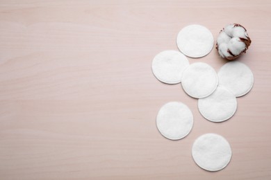 Many clean cotton pads and flower on wooden table, flat lay. Space for text