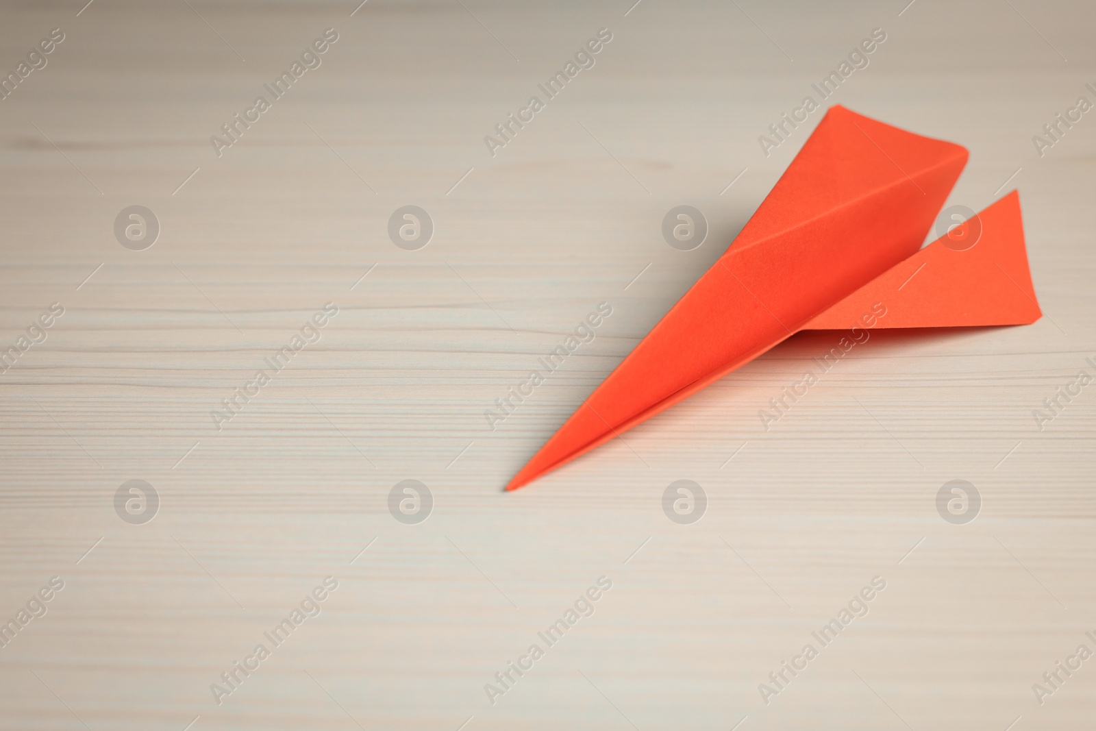 Photo of Handmade orange paper plane on beige wooden table. Space for text