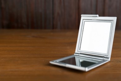 Photo of Stylish cosmetic pocket mirror on wooden table. Space for text