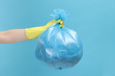 Photo of Woman holding plastic bag full of garbage on light blue background, closeup