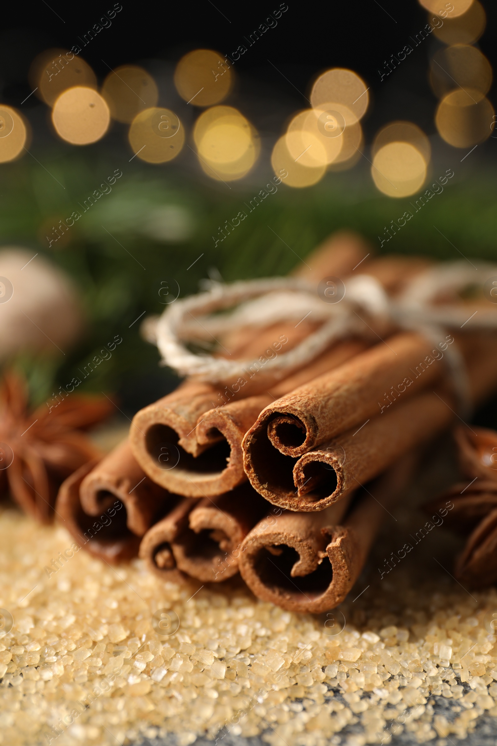 Photo of Different spices. Cinnamon sticks and cane sugar on table against blurred lights, closeup