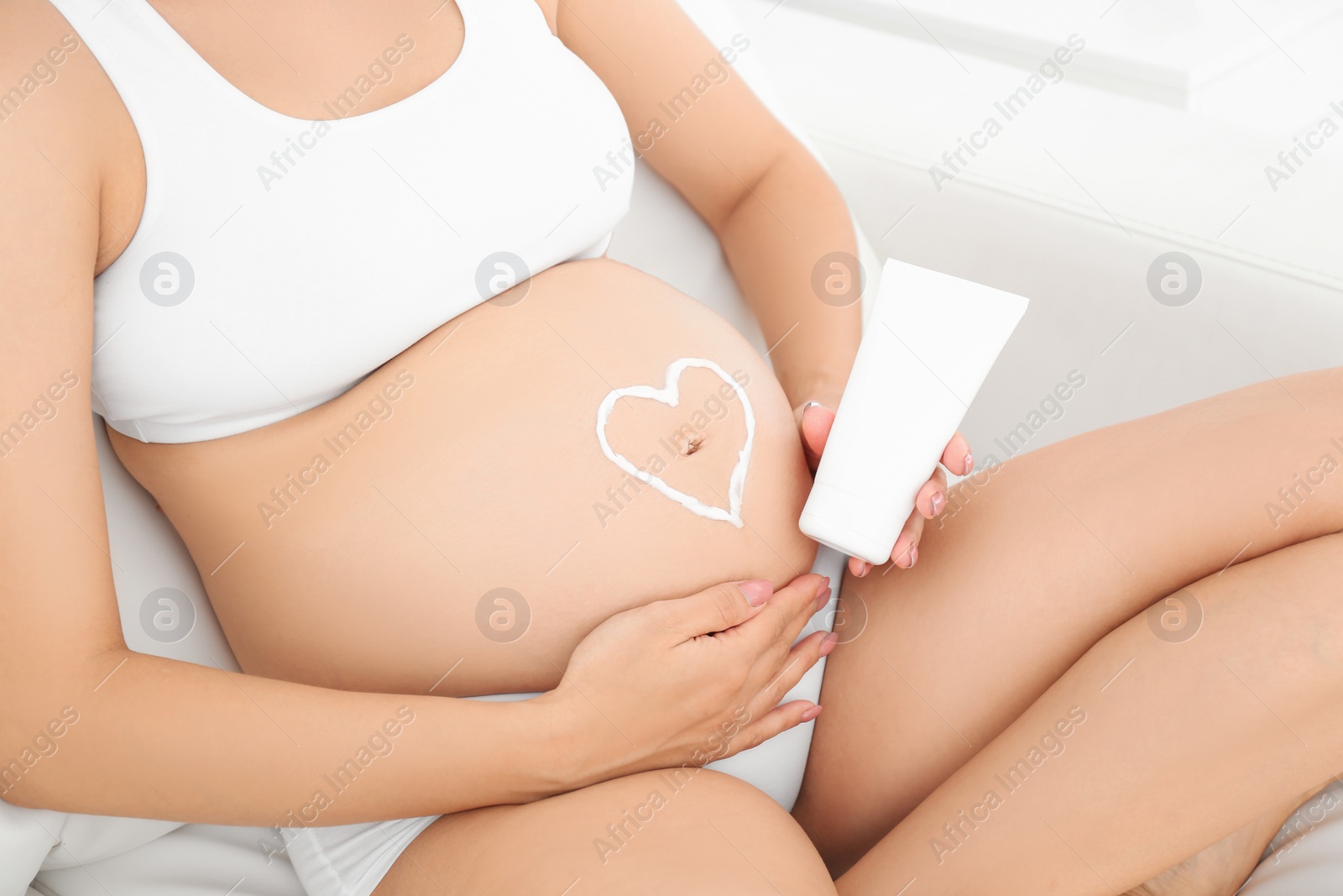 Photo of Heart painted with body cream on pregnant woman's belly at home, closeup