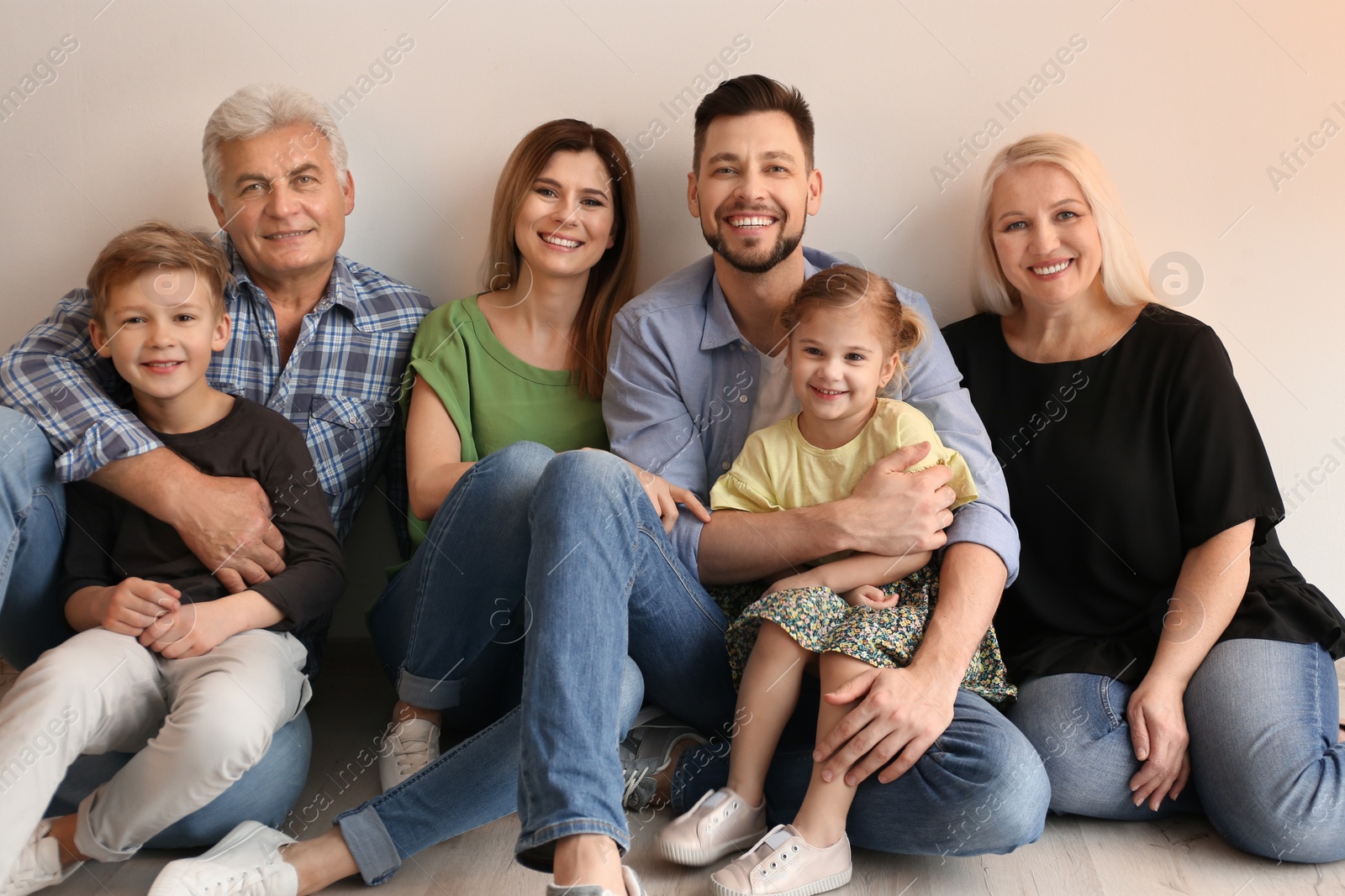 Photo of Happy family with cute kids sitting on floor near light wall