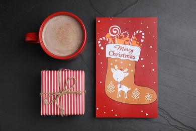 Photo of Christmas card, gift box and cup of cocoa on black background, flat lay