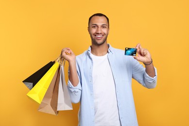 Happy African American man with shopping bags and credit card on orange background
