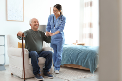 Photo of Care worker helping elderly man with stick in geriatric hospice