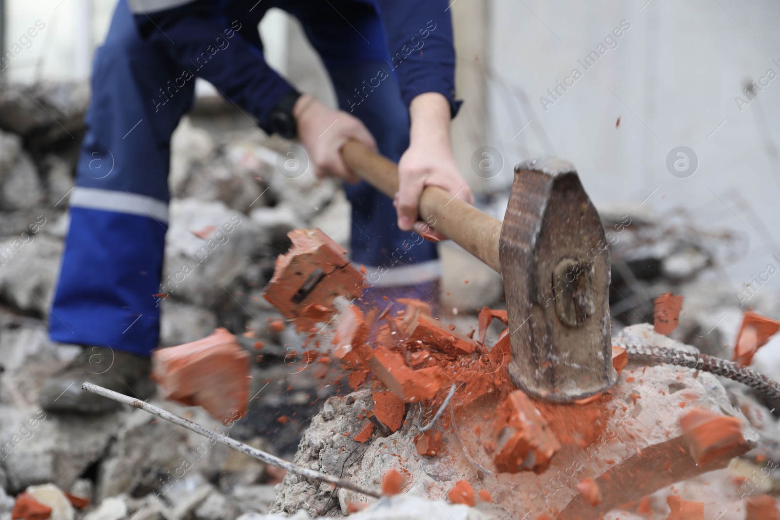 Photo of Man breaking brick with sledgehammer outdoors, selective focus