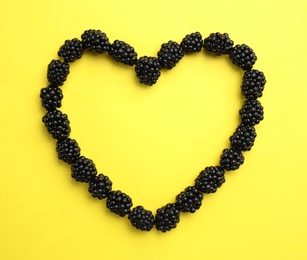 Photo of Heart shaped frame of ripe blackberries on yellow background, flat lay. Space for text