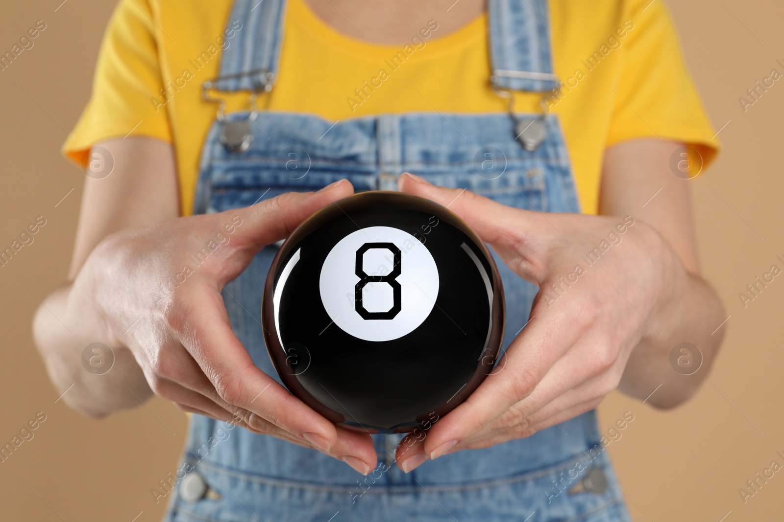 Photo of Woman holding magic eight ball on light brown background, closeup