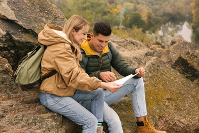 Couple of travelers with backpacks and map on rocky mountain. Autumn vacation