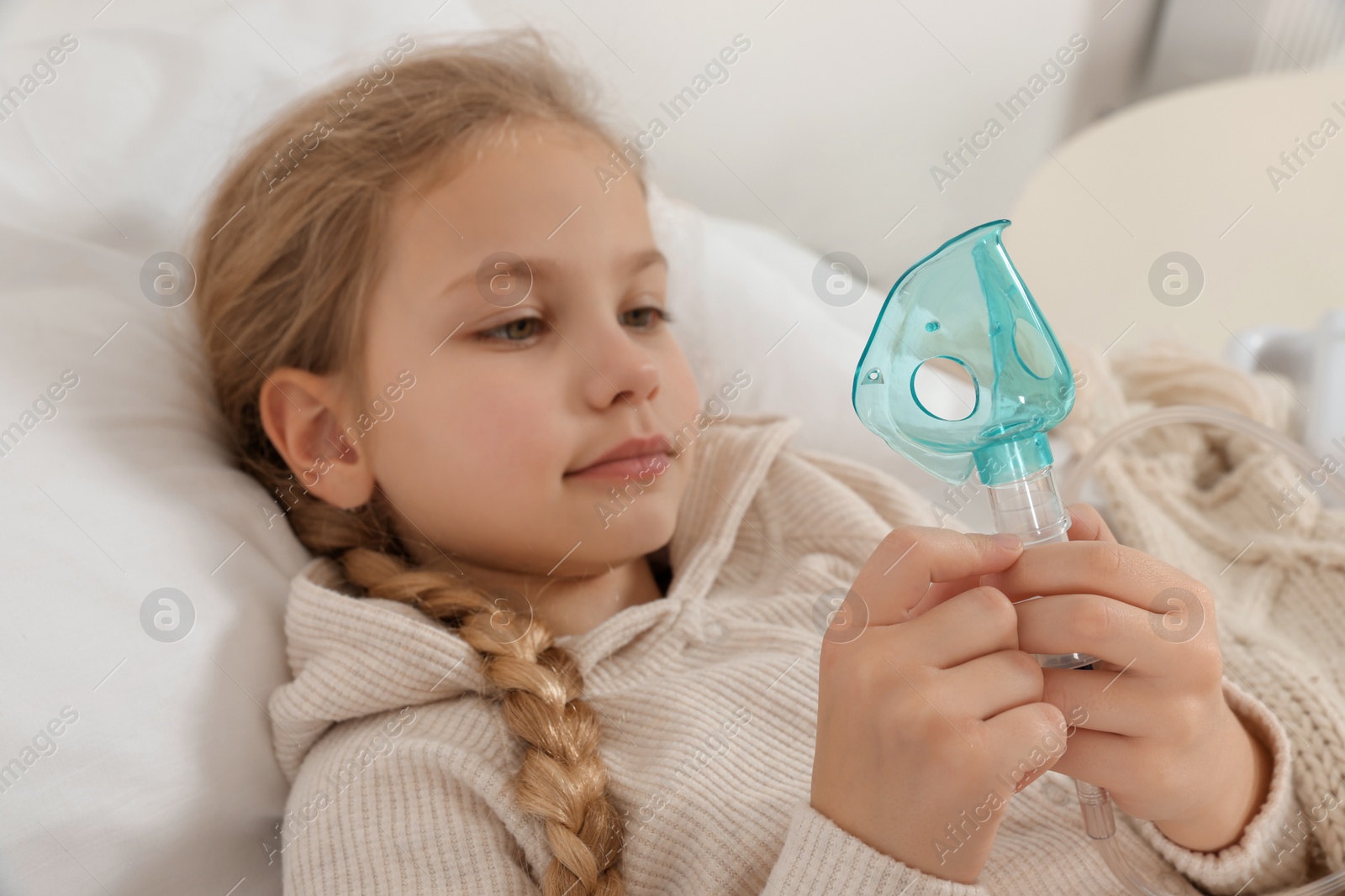 Photo of Little girl holding nebulizer for inhalation on bed at home