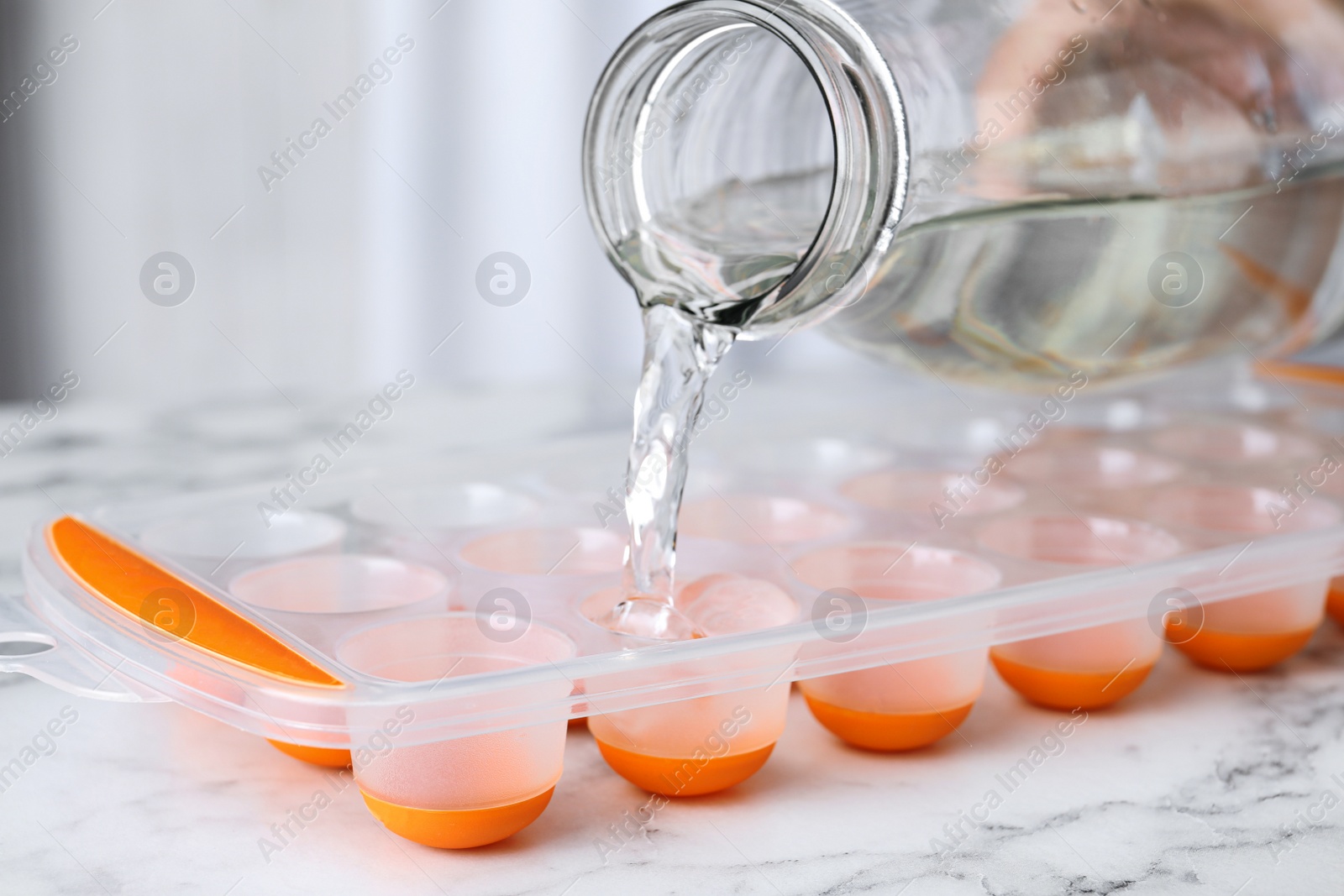 Photo of Pouring water into ice cube tray on white marble table, closeup