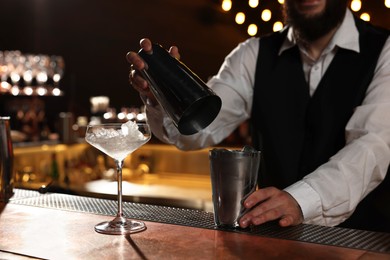 Bartender with shaker making fresh alcoholic cocktail at bar counter, closeup