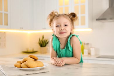 Cute little girl at table with cookies in kitchen