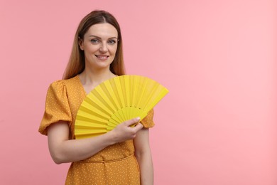 Happy woman with yellow hand fan on pink background, space for text