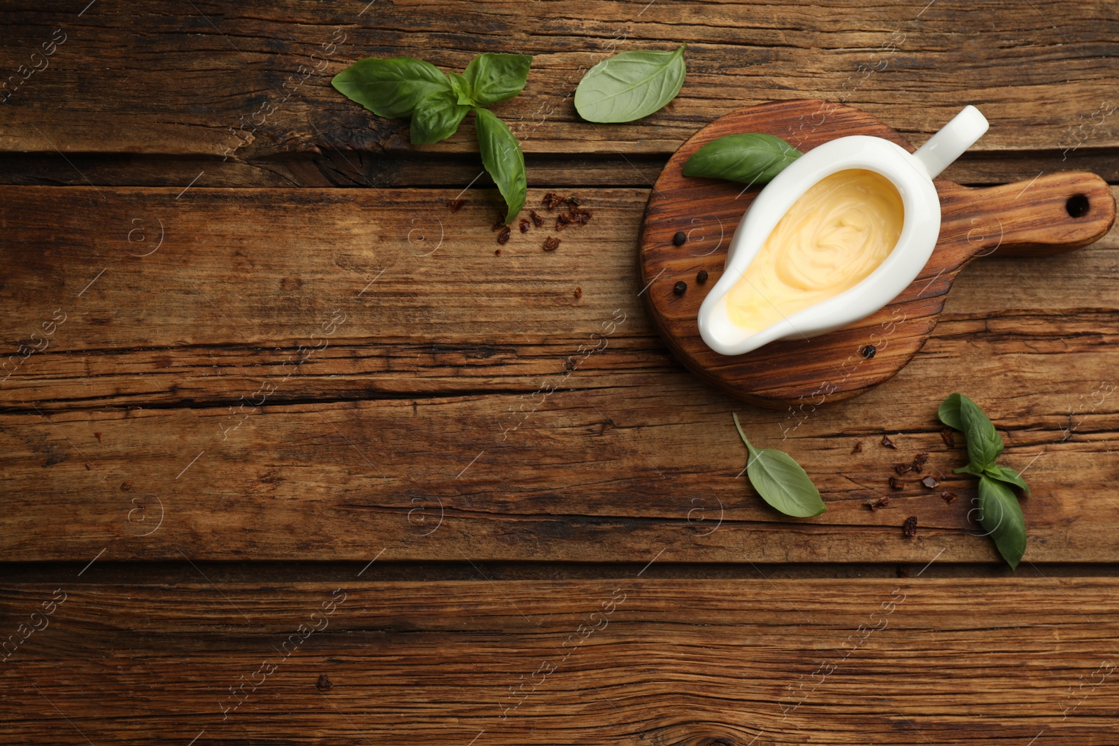 Photo of Tasty sauce in gravy boat, basil leaves and spice on wooden table, flat lay. Space for text