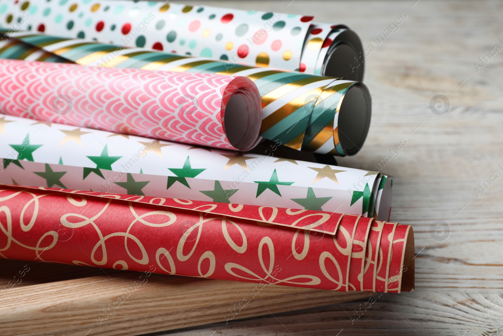 Photo of Different colorful wrapping paper rolls on white wooden table, closeup