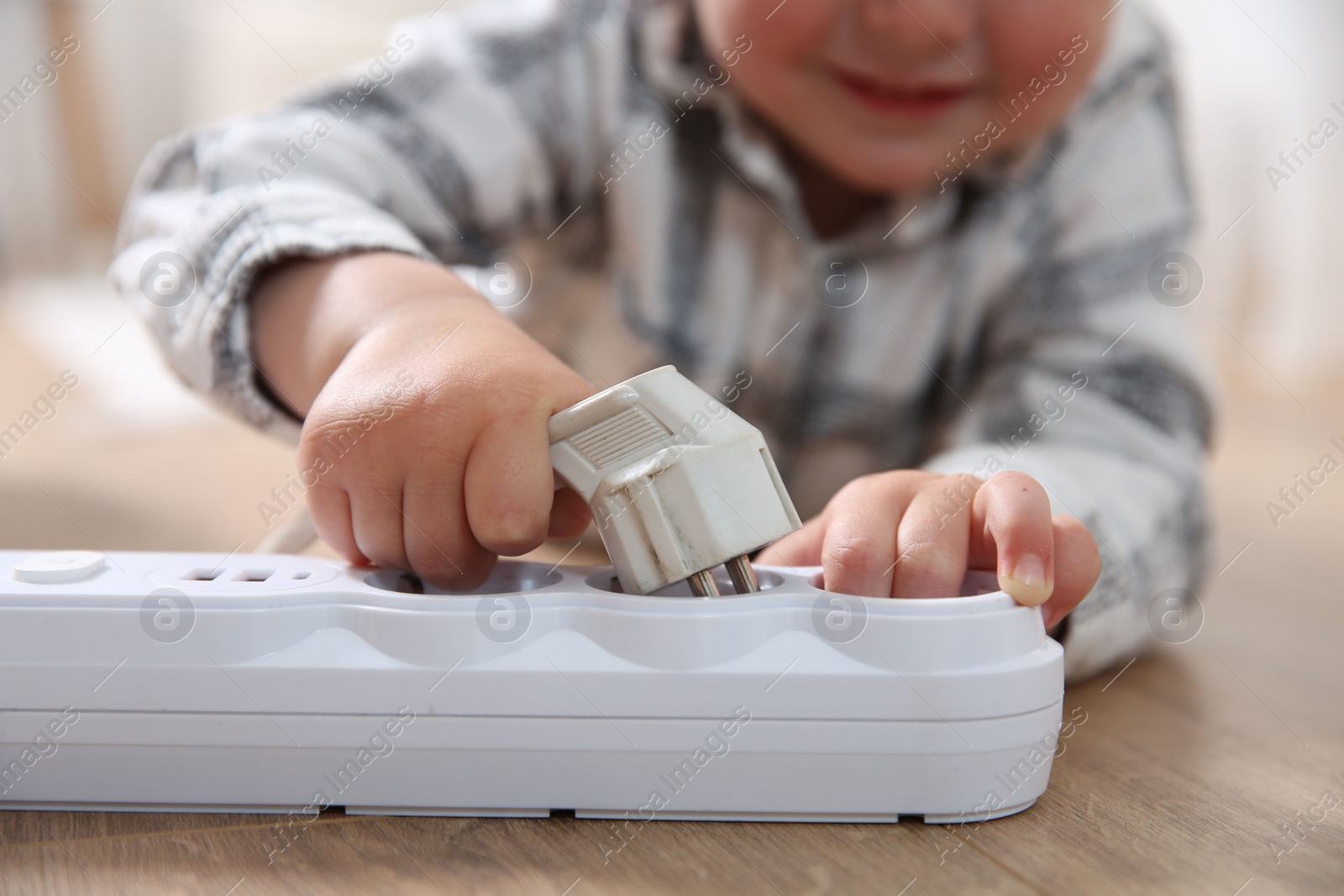 Photo of Little child playing with power strip and plug on floor indoors, closeup. Dangerous situation